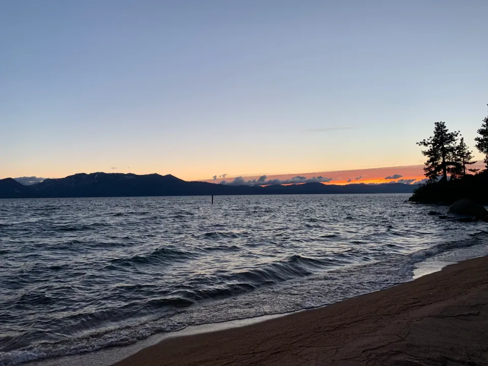 Lake Tahoe at sunset, orange horizon over mountains and calm water