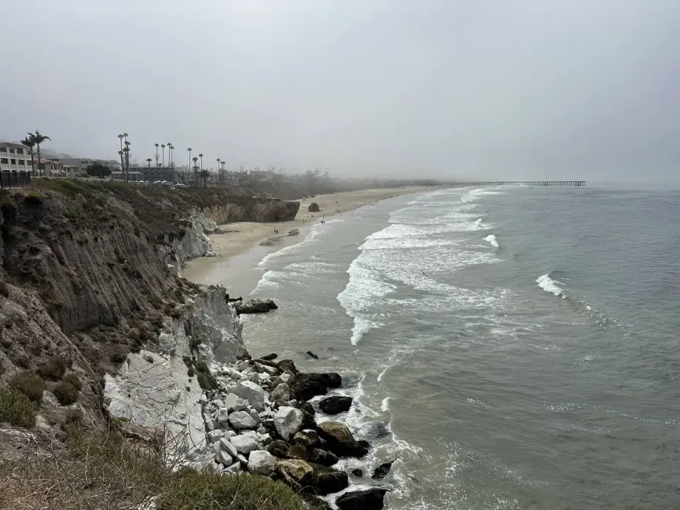 Surf and pier through coastal fog below a bluff