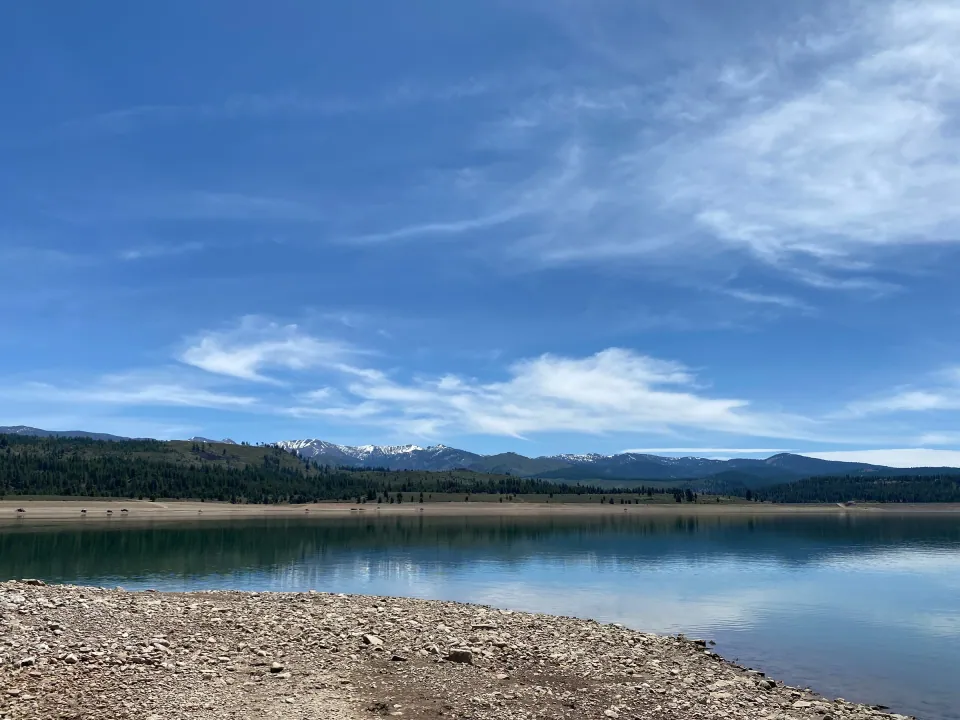 Calm mountain lake below forested ridges and distant snowy peaks