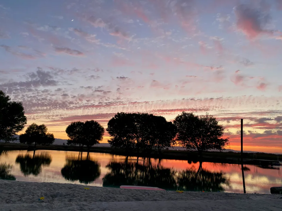 Pink sunset sky with tree silhouettes reflected in still water