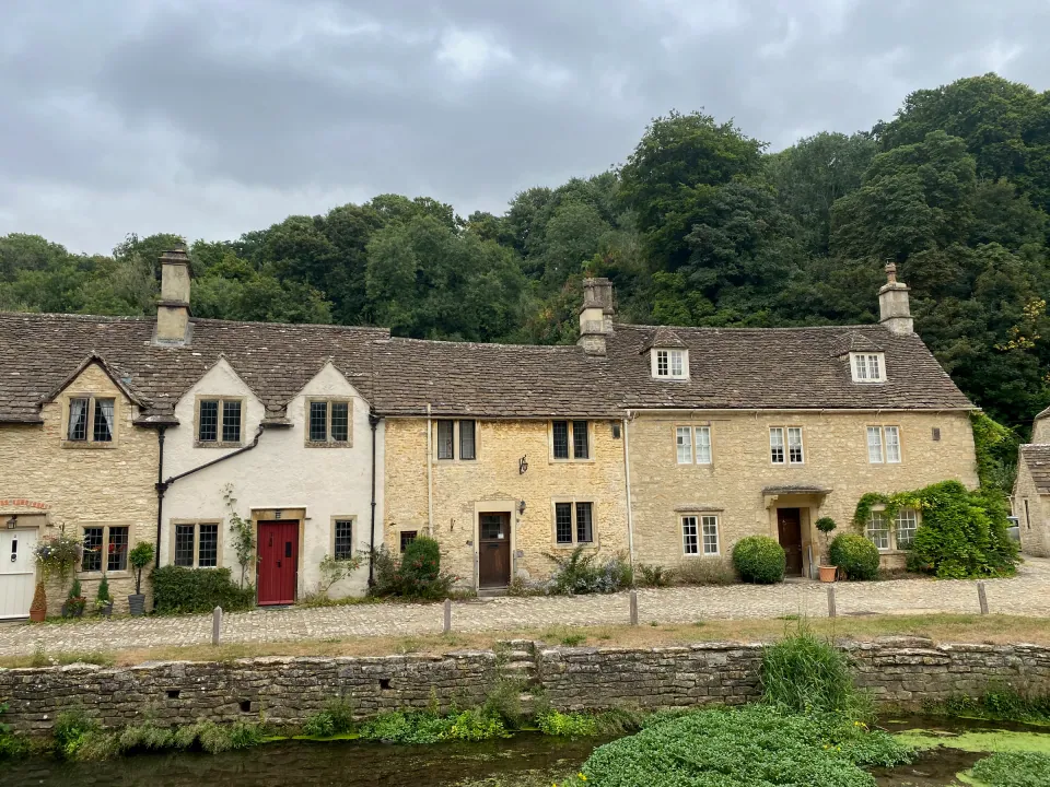 Row of Cotswold stone cottages above a green stream bank