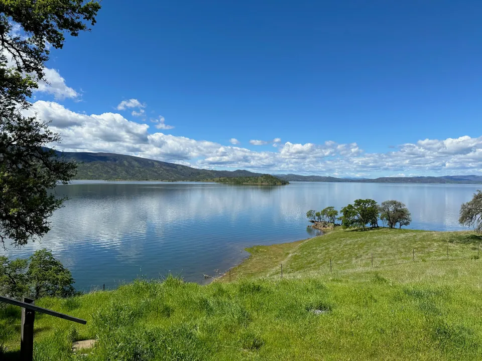 Wide blue lake below green grassy shore and puffy clouds