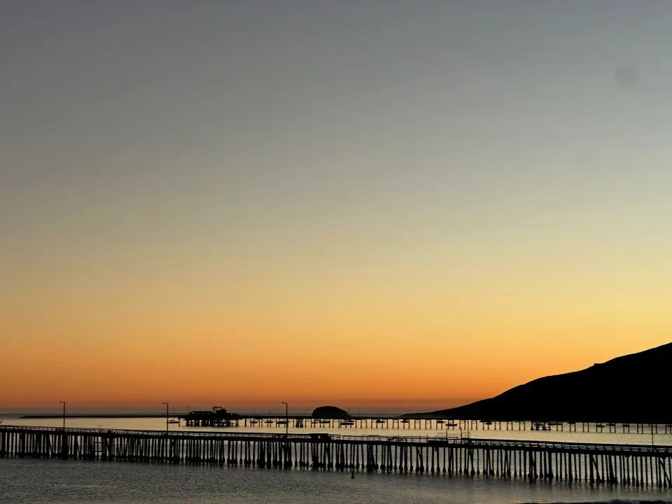 Orange twilight sky over pier and headland silhouette at the beach