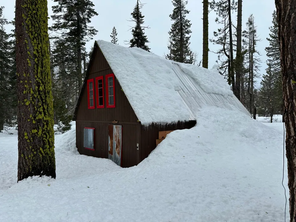 Red-trimmed A-frame cabin buried in deep snow among pines