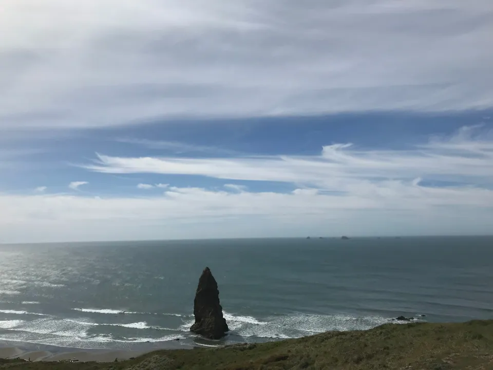 Lone sea stack off bluff on calm ocean, soft clouds