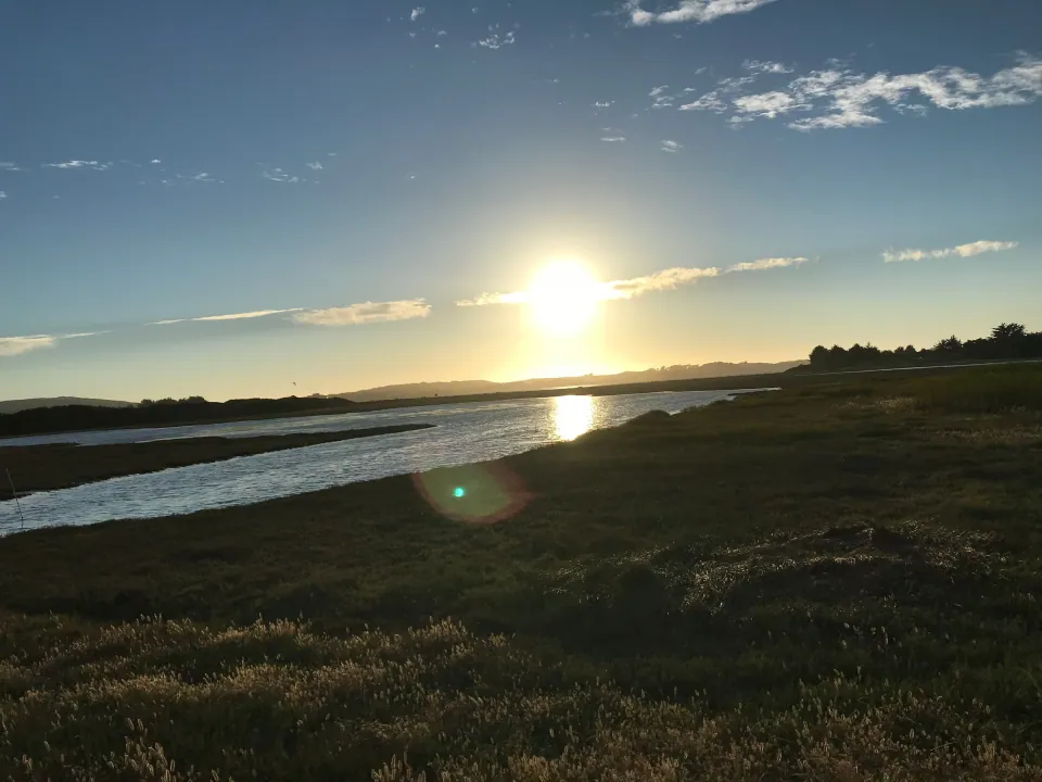 Low sun glowing over winding marsh slough and bay