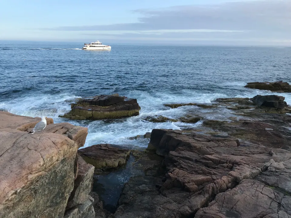 Waves on pink granite rocks, boat on deep-blue sea
