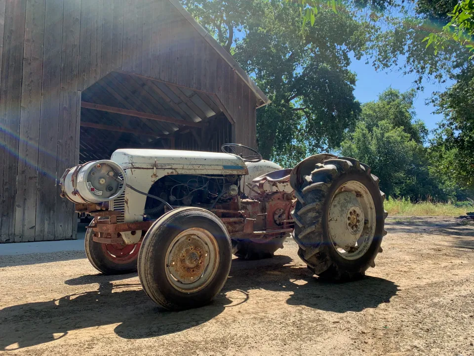 Vintage grey Ford tractor beside barn in summer sun