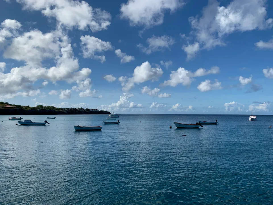 Small boats moored in calm blue bay under puffy clouds