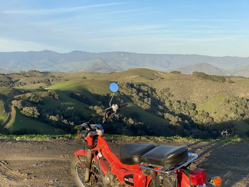 Red motorbike parked on a ridge above green canyons