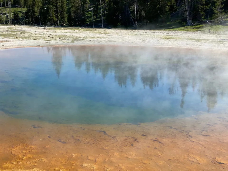 Yellowstone hot spring with orange rim reflecting blue sky
