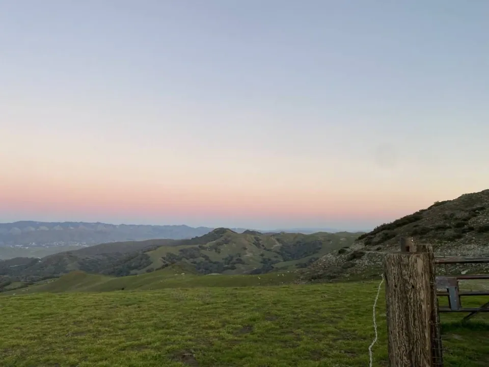 Pastel evening sky above green hills and a ranch gate