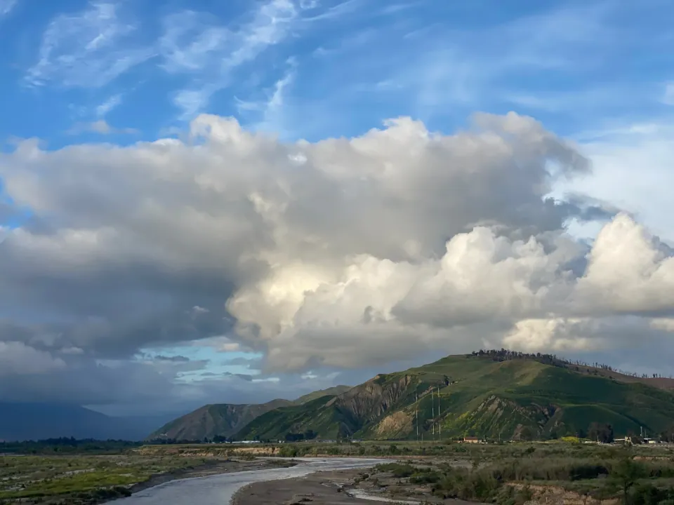 Towering storm clouds over green coastal ridge and creek