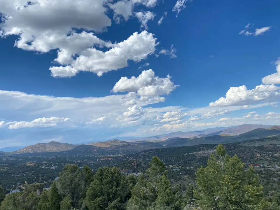 Puffy clouds over pine-forested valley and distant ranges