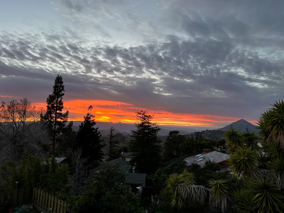 Fiery red sunset clouds over treetops and distant peak