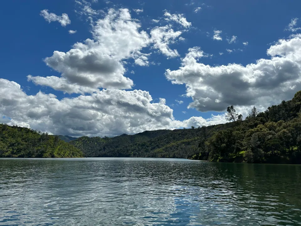 Clouds over forested hills rising from a reservoir