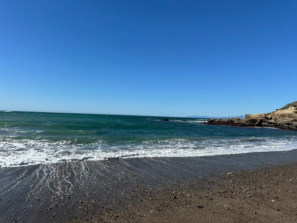 Blue surf rolling onto beach beside rocky headland