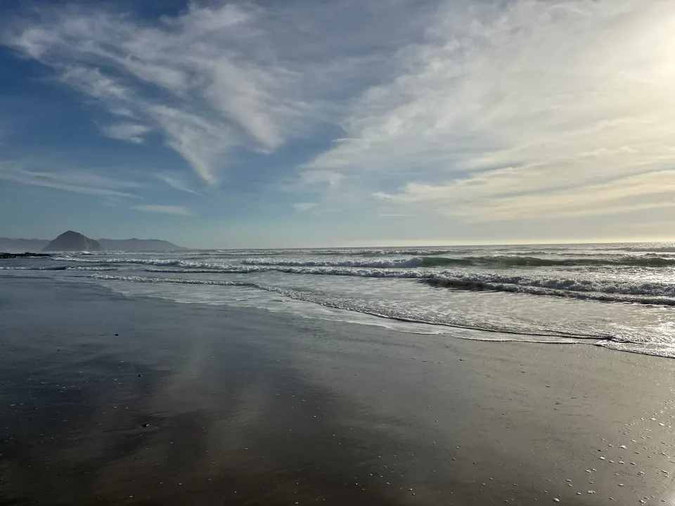 Wet sand reflecting sky with Morro Rock on the horizon