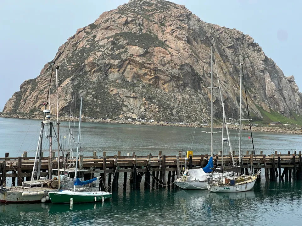 Morro Rock towering over harbor docks and moored sailboats