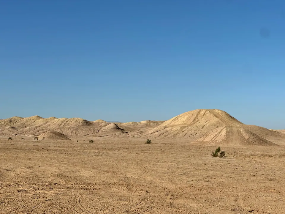 Sandy desert dunes and a tall dune under clear blue sky