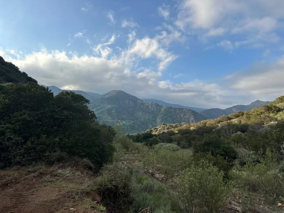 Chaparral canyon opening to distant mountain ridges under scattered clouds