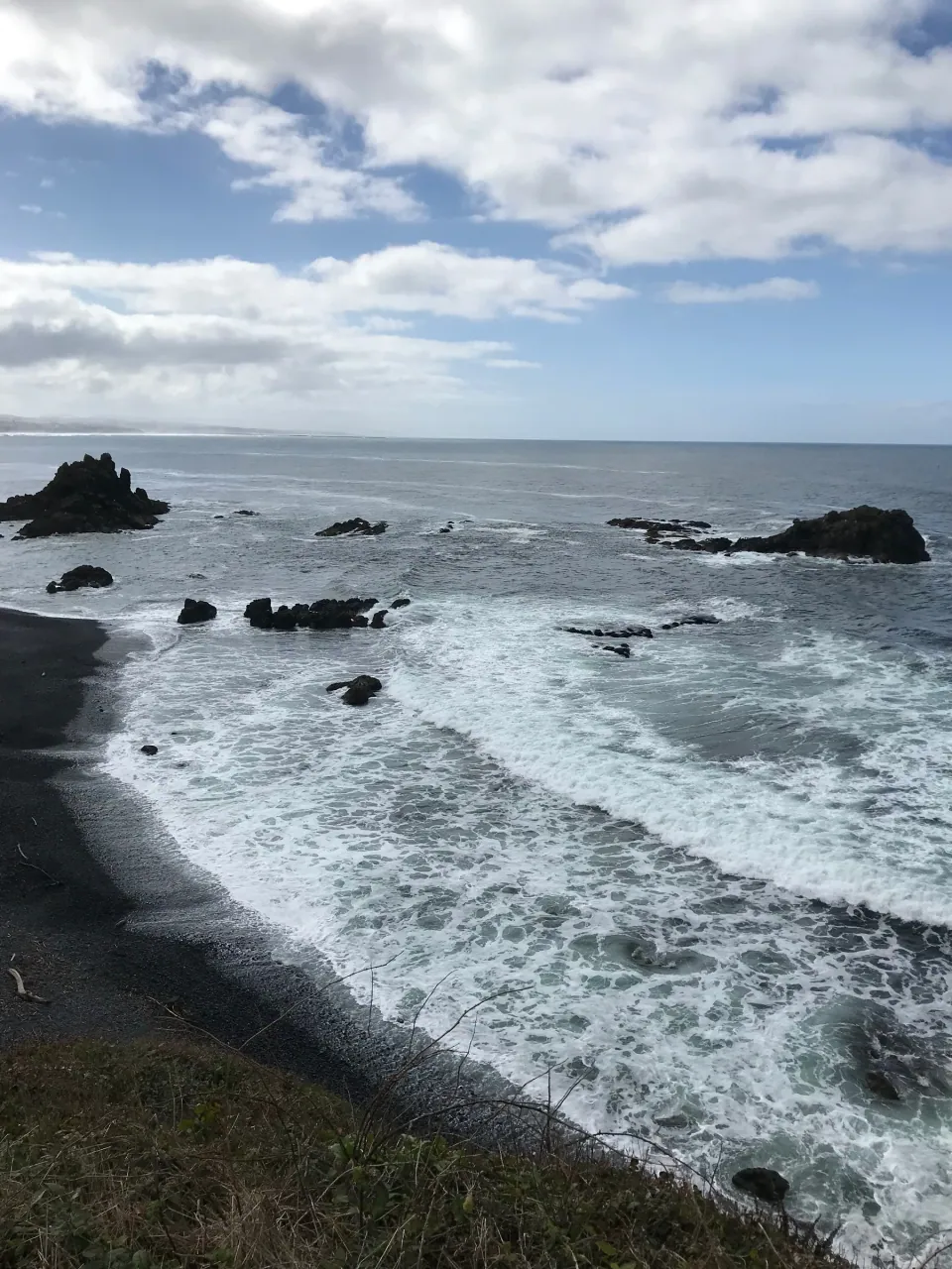 Black-sand beach and surf below dark sea stacks