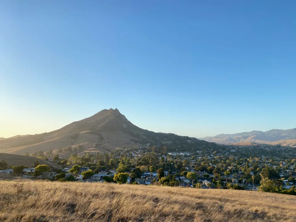 Volcanic peak in morning light above golden grass and rooftops