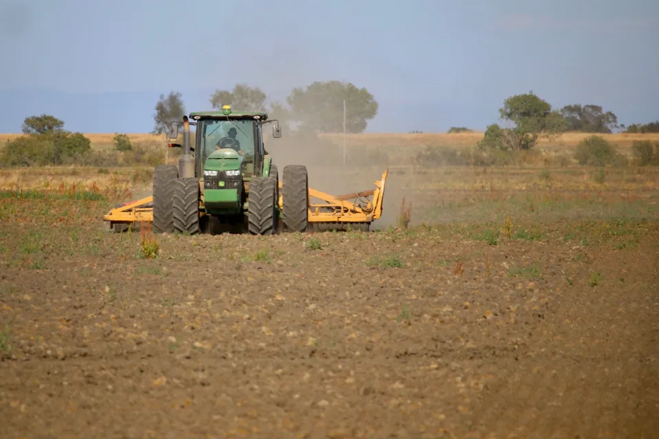 Green tractor pulling a harrow through a dusty field