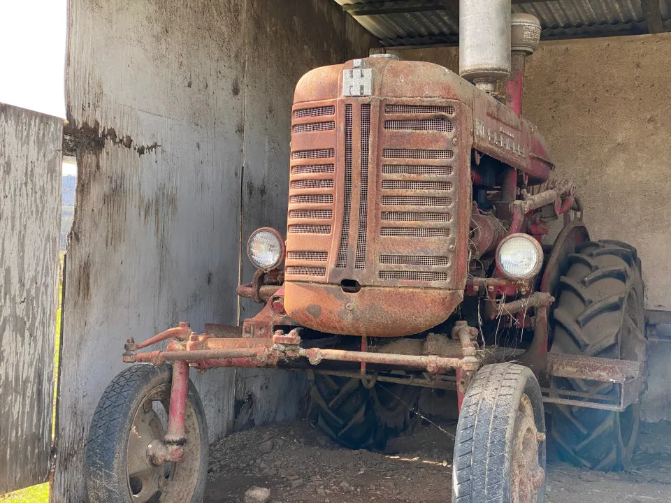 Old red International tractor in the shade of a barn