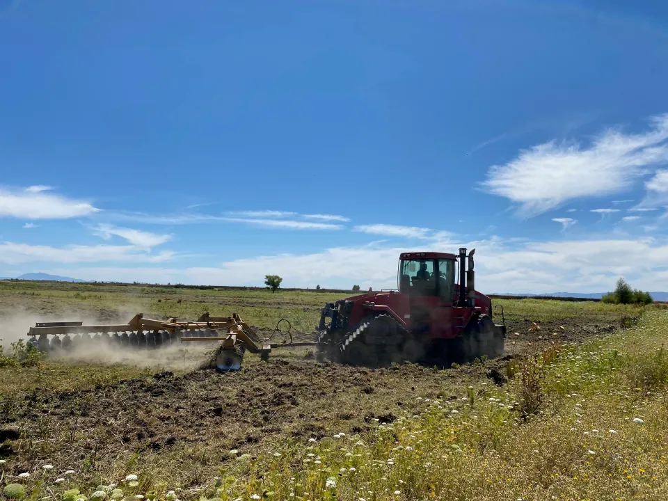 Tractor discing a field under a blue sky