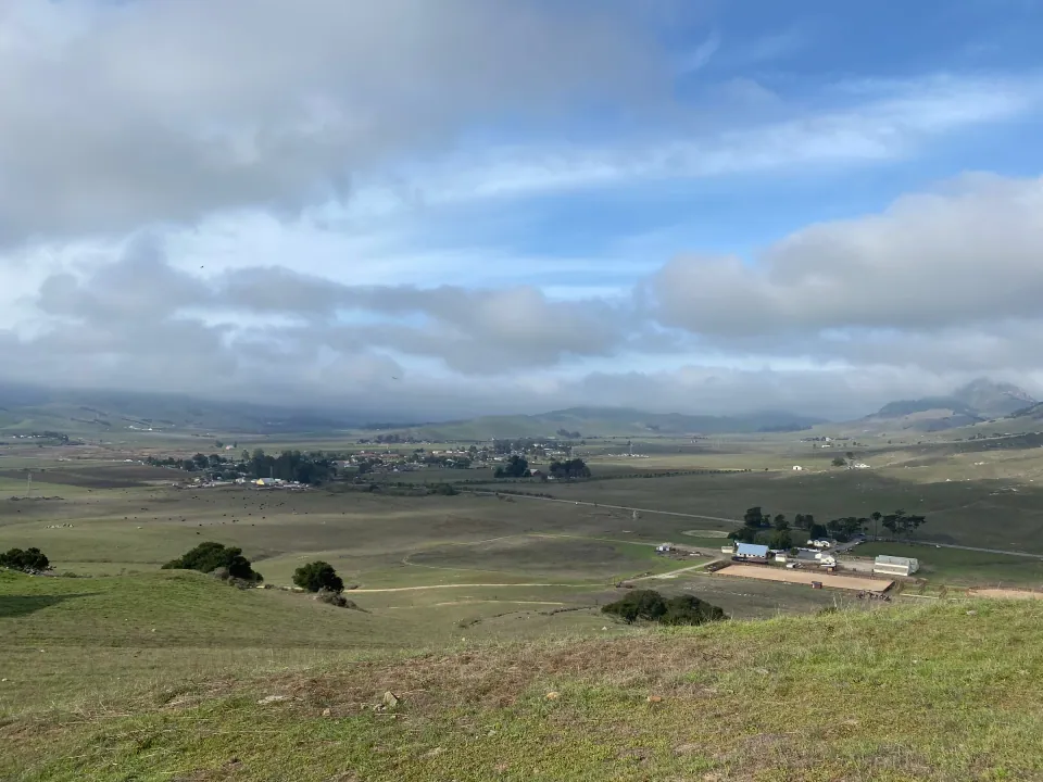 Ranch buildings in a broad green valley under clouds
