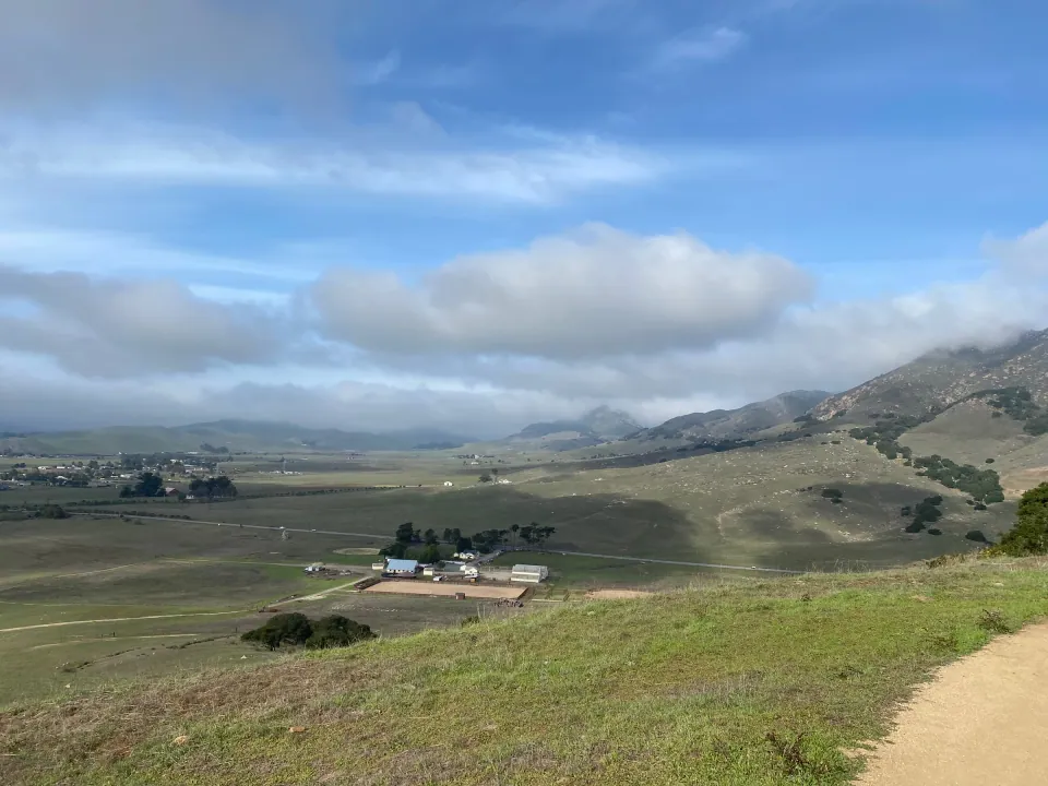 Ranch in a green valley below cloud-topped hills