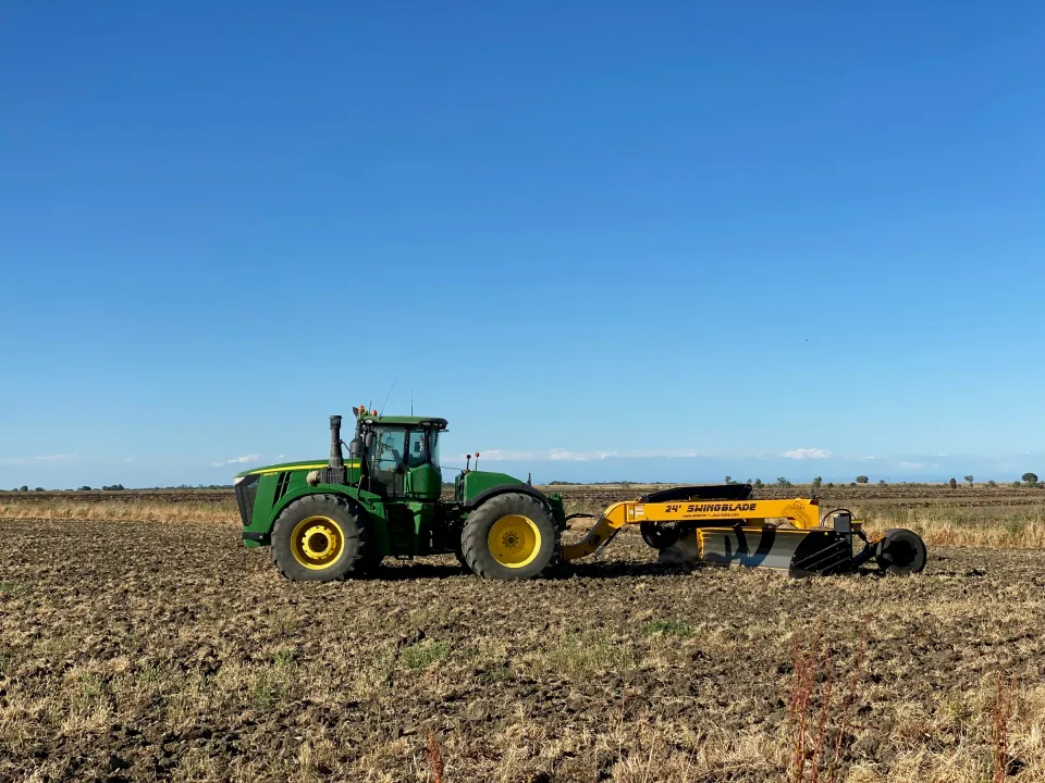 Green tractor pulling a scraper across a bare field