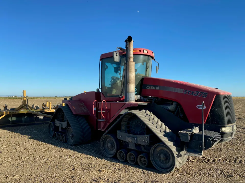 Red track tractor hitched to a disc in a bare field