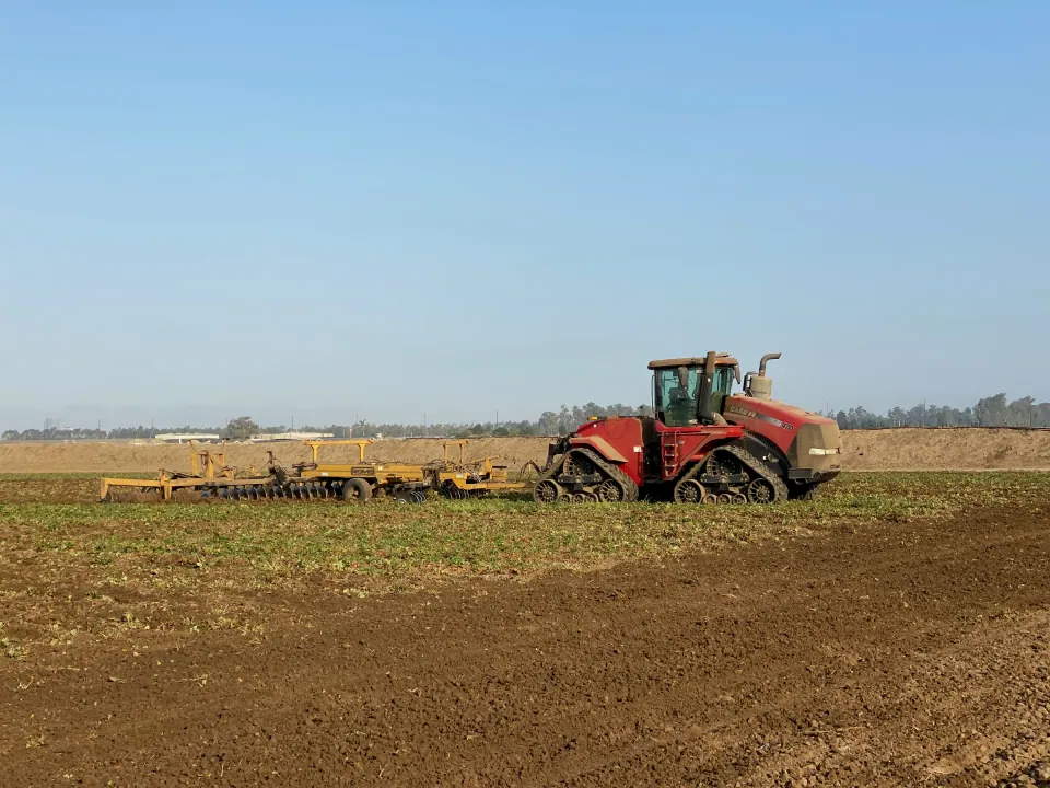 Track tractor pulling a seeder across a plowed field